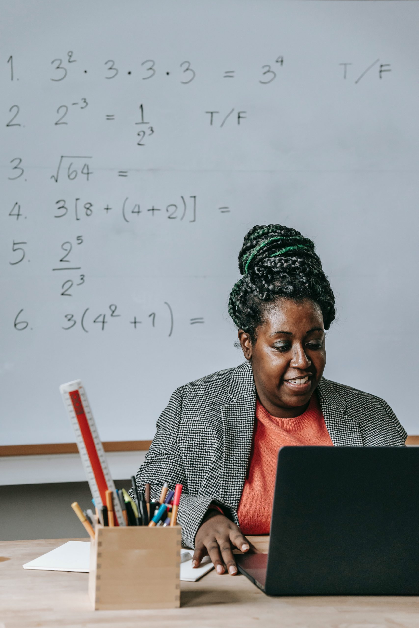 Black woman sitting at desk with laoptop with whiteboard of equations behind her