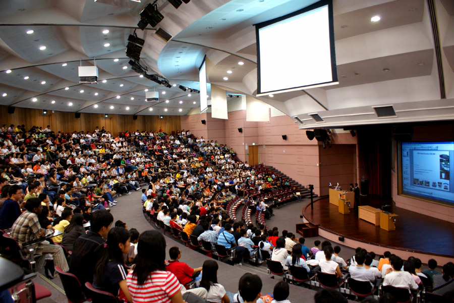 Instructor presenting to hundreds of students in a large lecture hall.