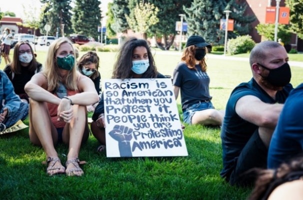 group of people sitting in the grass with one woman holding an anti-racism sign