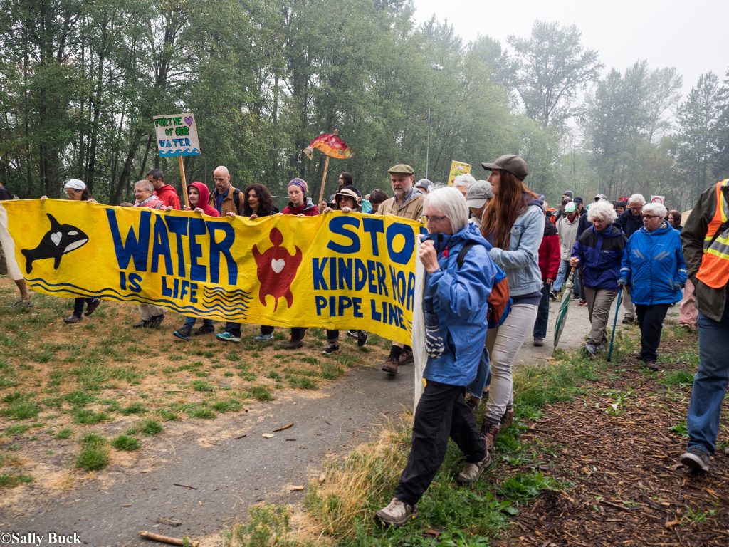 Protesters on forest road carrying banner that says water is life and stop Kinder Morgan pipline.