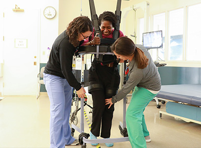 Photo showing two therapists providing rehabilitation to a patient in a harness