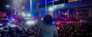 Young person with raised fist standing in front of a crowd and police