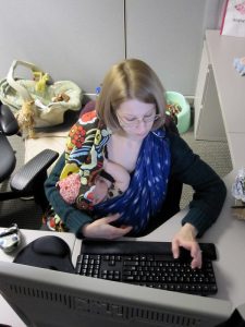 Mother working at a computer and breastfeeding a child.