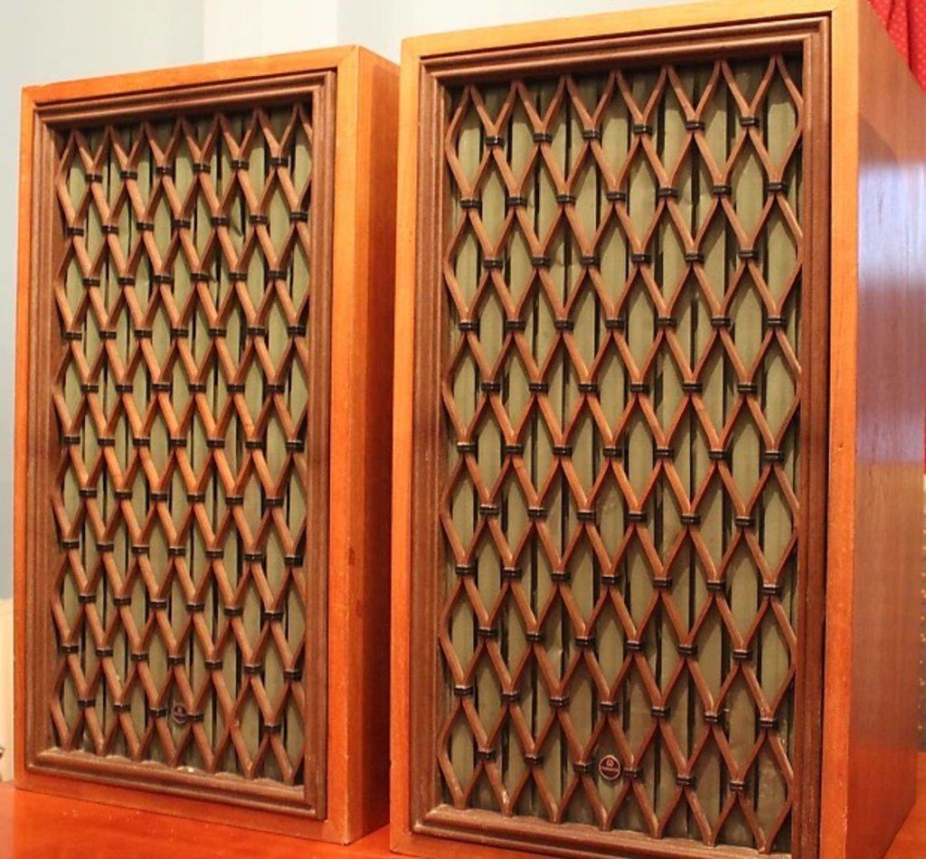 Two old stereo speakers in wood cabinets. The speaker grills are an ornate lozenge pattern, resembling the fireplace grate and the lattice-like layer of cut paper on the green shown earlier.