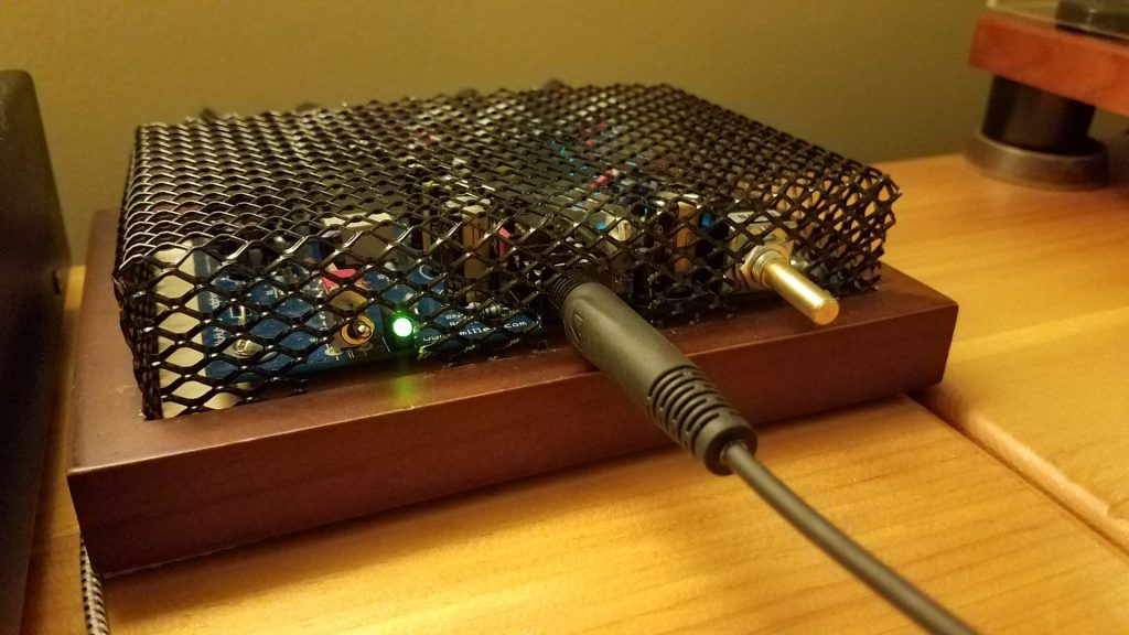 Headphone amplifier made with a wooden base and a black metal screen top.