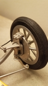 Close-up of a model car front wheel assembly. Axl, brake rotor, caliper, and tie-rod are visible.