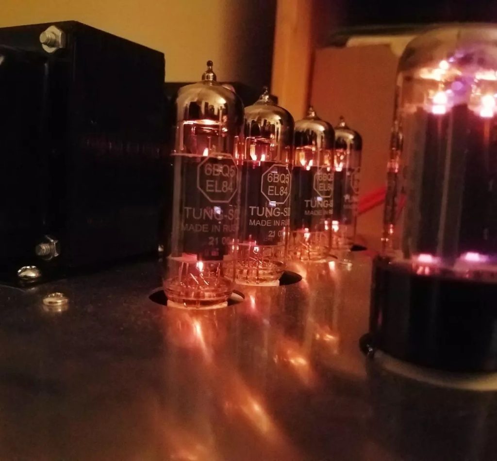 Close-up of amplifier with vacuum tubes glowing in low lighting.