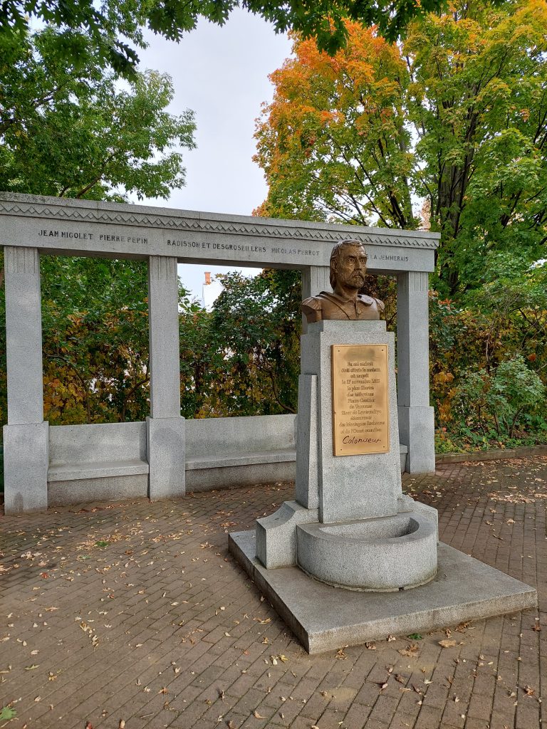 Monument featuring a bust on a concrete pedestal adorned with a plaque, and four columns behind it.