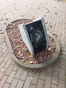 Lamp within a concrete block angled at about 45 degrees, with black scribbles over the plastic covering the light bulb.