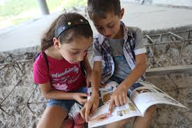 a young boy and a young girl sit next to each other reading a book together