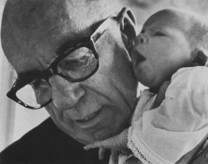A black and white photo of Dr Spock, an old man, holding a baby.