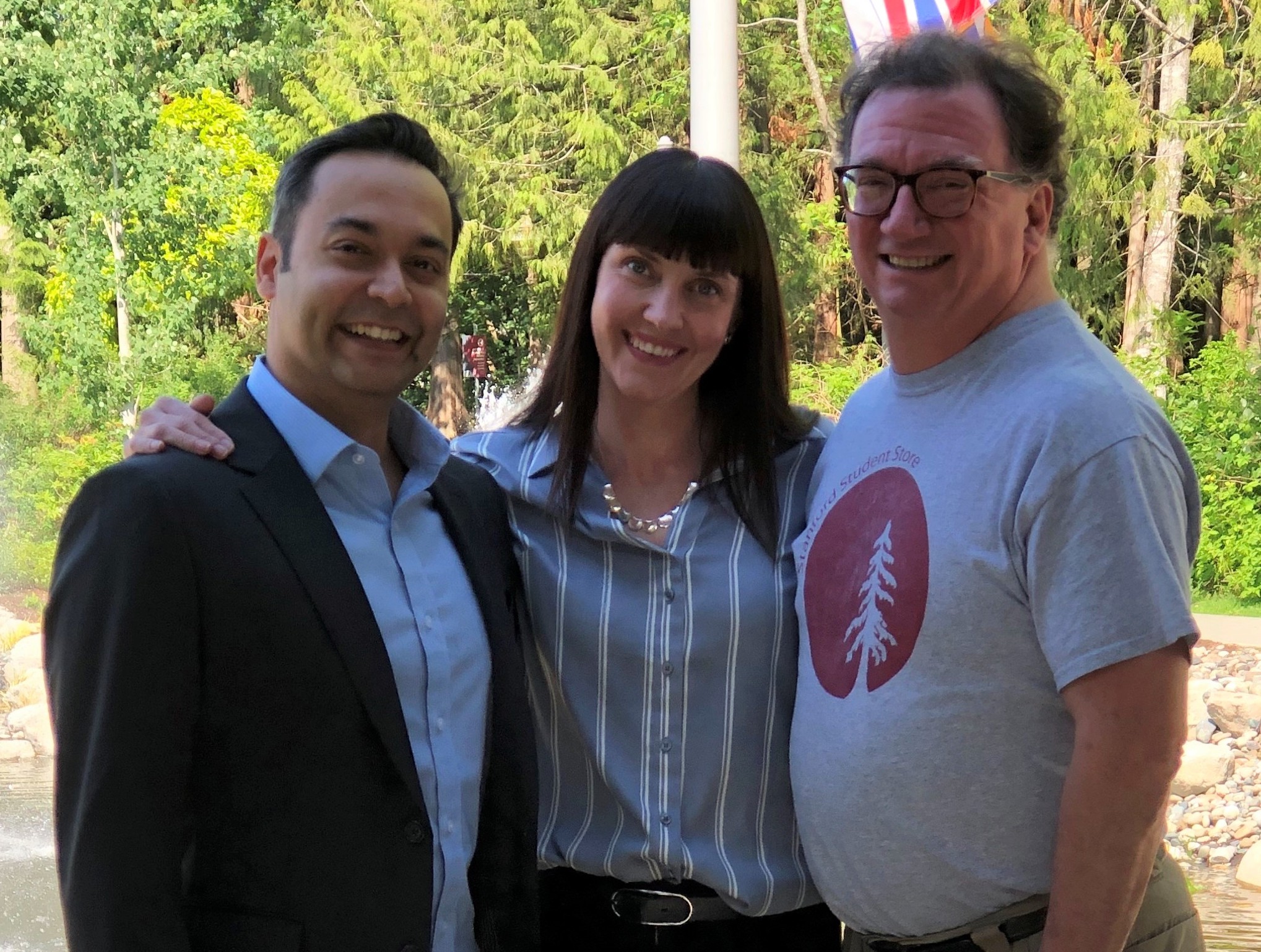 Rajiv Jhangiani, Carrie Cuttler, and Dana Leighton smiling while standing in front of greenery and a partly-obstructed flag pole.